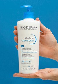 Bioderma Atoderm Crème Ultra, flacon en plastique blanc avec pompe, accents bleus, 500 ml, présente des détails sur la crème hydratante dans plusieurs langues.