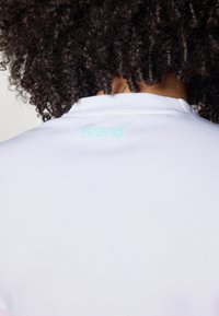 White athletic shirt with a textured fabric, featuring a light blue embroidered "Island" logo at the back neckline.
