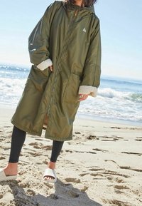 Oversized frakke i olivengrøn med fleeceforede ærmekanter, forlommer og hætte, lynlåslukning og minimal branding.