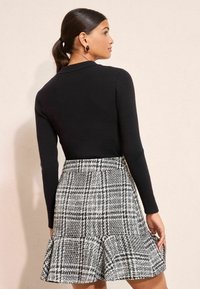 Fekete bordázott hosszú ujjú felső, szürke és fehér kockás harangszoknyával, amely fodros szegéllyel rendelkezik. Simasága és letisztult vonalai kiemelik a ruhadarabok textúráját.