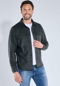Gray plaid shirt with a button-up design, two chest pockets, and a collar, paired with a white crew-neck t-shirt and blue jeans.