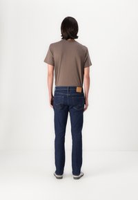 Tricou scurt cu mânecă maro, asortat cu blugi de denim de culoare albastru închis, având o patch din piele pe spate și croială standard dreaptă.