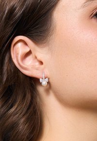 Srebrne kolczyki w kształcie łuku z perłowym wiszącym elementem, z teksturowanym wzorem, błyszczącymi akcentami i wypolerowanym wykończeniem.