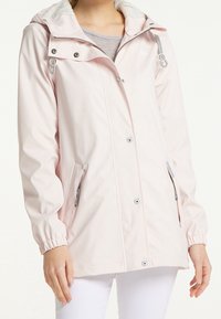 Veste imperméable rose clair avec capuche, équipée de boutons-pression argentés, de poignets élastiques et de poches latérales avec fermetures éclair transparentes.