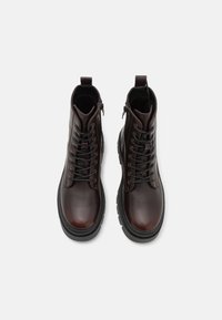 Botine maro din piele, cu sireturi și fermoare pe lateral. Au vârful rotunjit și talpa groasă de culoare neagră. Textură netedă, fără modele vizibile.