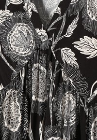 Schwarzer Stoff mit einem weißen Blumenmuster, das detaillierte Sonnenblumen und Blätter zeigt. Weiche Textur mit einem Wickeldesign und Falten.