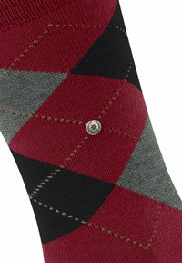 Calzino con un motivo argyle rosso, nero e grigio, con piccoli dettagli di cucitura e un'emblema metallico rotondo del marchio.