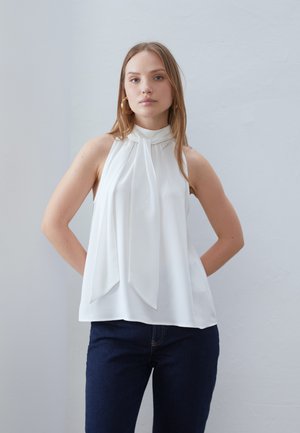Hvid udenærmet top med høj hals og plisseret frontdesign. Glat stof med løs pasform, parret med mørke denim jeans.