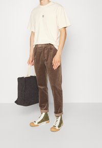 Beige t-shirt met korte mouwen met een zwart "II" grafiek, bruine corduroy broek, groene hoge sneakers met witte accenten, met een zwarte tote-tas.