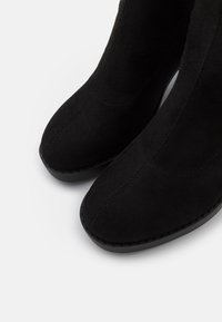 Bottes cheville en daim noir avec un design à bout pointu. Présentent une texture lisse, des accents de couture et une semelle basse en caoutchouc.