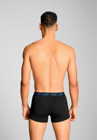 Black boxer shorts with a blue Puma logo waistband, viewed from the back. Material appears smooth and stretchy. Skin is visible above the shorts.