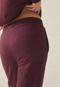 Bordeaux svedbukser med elastisk talje og en baglomme. Glat tekstur med en tætsiddende design, der fremhæver taljen.
