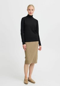 Un pull noir à col montant avec des manches longues associé à une jupe midi marron côtelée. Le mannequin porte des slip-ons beiges. Les textures contrastent entre les vêtements.