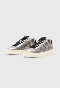 Un paio di sneaker basse con punte metallizzate argento, lati in stampa serpente, lacci neri e suole chunky bianco sporco su uno sfondo grigio chiaro.