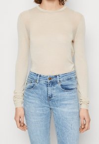 Beige dlouhý rukáv top s kulatým výstřihem a strukturovaným povrchem, v kombinaci s světle modrými džínami s klasickým pětipocket designem.