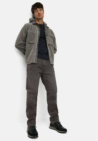 Gray corduroy jacket with a hood, black shirt, and dark gray jeans. Black lace-up shoes with textured soles. Two chest pockets on the jacket.