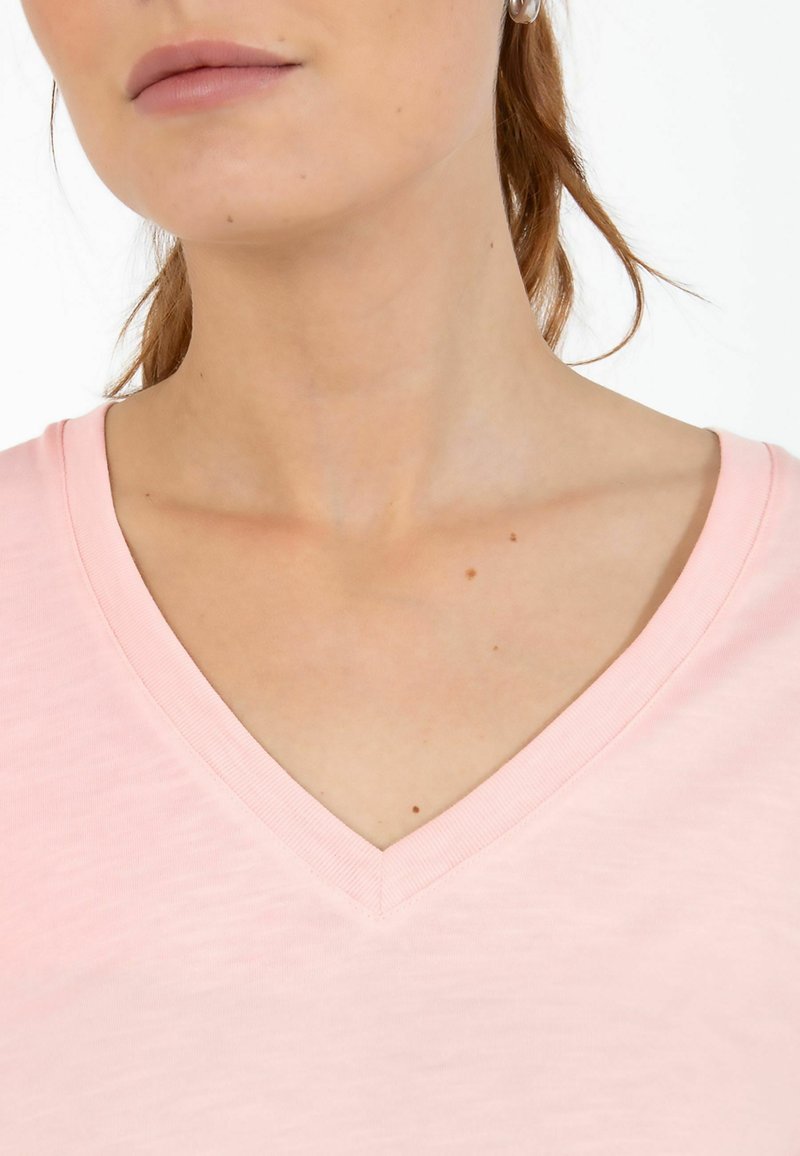 T-shirt rose clair à col en V, doté d'une texture douce, d'un motif chiné subtil et d'une coupe décontractée, parfait pour un usage quotidien.