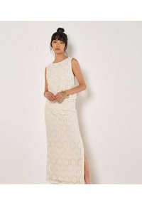 Robe en dentelle ivoire avec des motifs hexagonaux. Design sans manches, longueur maxi avec une fente sur le côté et des textures détaillées tout au long.