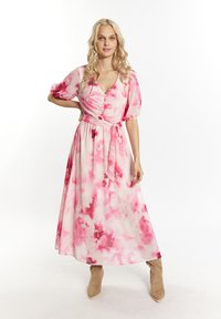 Maxi dress floreale rosa con maniche a sbuffo, scollatura a V, vita segnato e una gonna fluida; abbinata a stivali ankle beige con punta a punta.