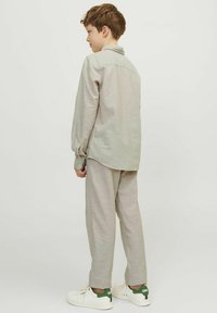 Maglietta a maniche lunghe grigia chiara con dettagli di bottoni e pantaloni grigi chiari abbinati; vestibilità casual, texture morbida, abbinata a sneaker bianche.