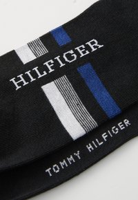 Fekete pamut zoknik fehér és kék csíkokkal, a „HILFIGER” és a „TOMMY HILFIGER” logók kontrasztos fehér szöveggel.