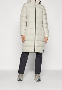 Puffjacka i ljusgrått, med en hel frontdragkedja, hög krage och sidofickor. Kombinerad med mörka byxor och ljusfärgade sneakers.