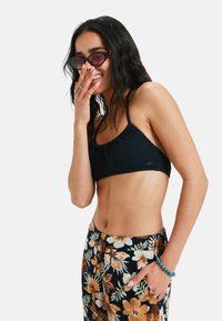 Navy blue textured bikini top with adjustable straps, paired with black floral patterned pants featuring white and orange flowers.