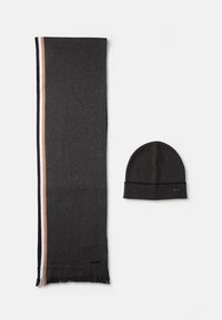 Foulard negru cu dungi laterale în alb, culoare brown deschis și brown închis, asociat cu o căciulă tricotată neagră asortată. Ambele articole au un etichetă.