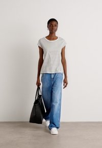 T-shirt a righe in tessuto leggero, abbinato a jeans blu larghi. Una borsa a tracolla nera e scarpe da ginnastica bianche completano l'outfit. Design semplice e casual.