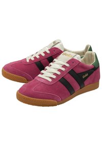 Sneaker in suede rosa con strisce nere e un tallone verde, caratterizzate da lacci bianchi e una suola in gomma strutturata color gomma. Il logo del brand è dorato.