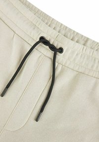 Helle beiges Shorts aus einem glatten Stoff; mit einem schwarzen Kordelzug und einer Fronttasche ausgestattet.