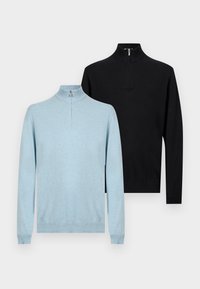 Δύο πουλόβερ μακρυμάνικα με φερμουάρ μέχρι τη μέση, ένα ανοιχτό μπλε μπροστά και ένα μαύρο πίσω, εκτεθειμένα σε απλό φωτεινό φόντο.