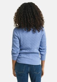 Helle blaue Pullover aus Grobstrick mit gerippten Bündchen und Saum, kombiniert mit dunkelblauen Jeans. Der Pullover weist ein strukturiertes Muster und eine figurbetonte Passform auf.