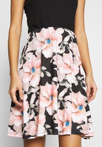 Bloemrok met een zwarte basis en grote roze en witte bloemen, benadrukt door blauwe centra. Gemaakt van zachte stof met een uitlopende vorm.