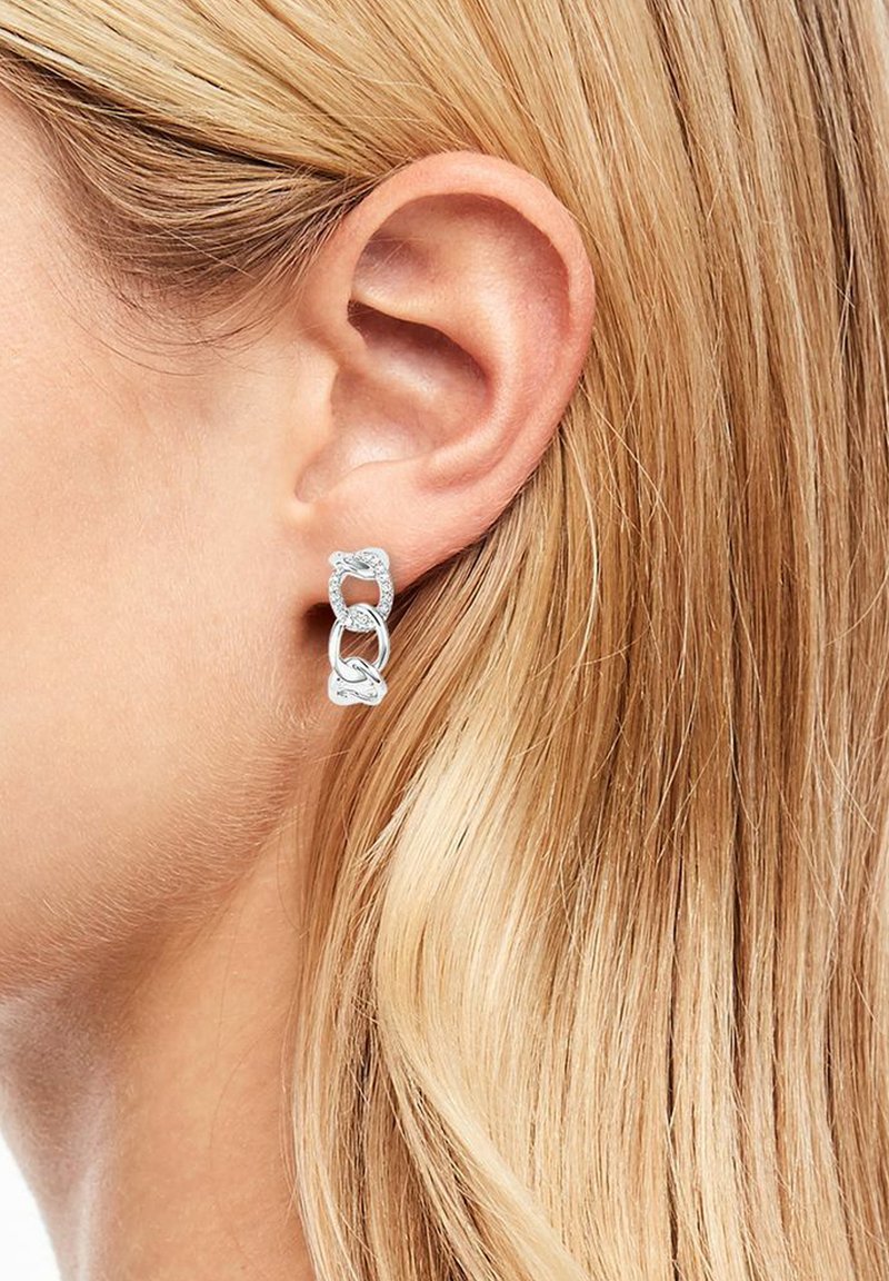 Silberne Kettenglieder Ohrringe mit drei miteinander verbundenen Gliedern, getragen am linken Ohr einer Person, mit blondem Haar im Hintergrund sichtbar.