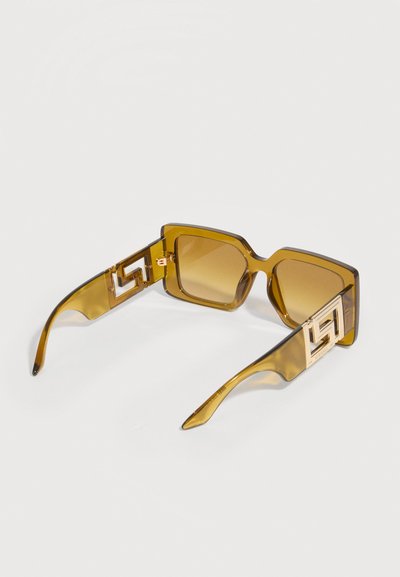 Γυαλιά ηλίου σε σχήμα τετραγώνου με κεχριμπαρένιο χρωματισμό, χοντρά διαφανή καφέ πλαίσια και χρυσές γεωμετρικές λεπτομέρειες λογότυπου στα δύο τμήματα των βραχιόνων.