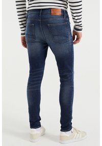 Mörk denim skinny jeans med en slät yta, fem fickor och en brun läderlapp i midjan. Subtilt slitdetalj på låren.