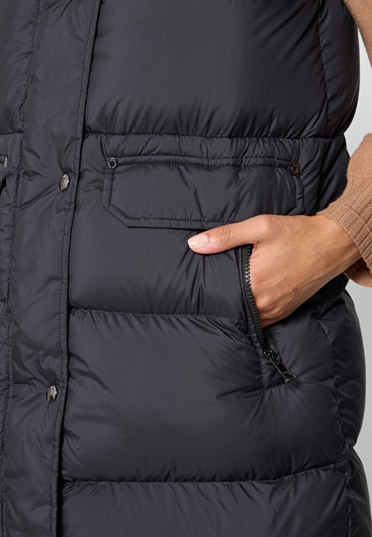 Schwarze Steppweste mit Reißverschlusstasche, Druckknöpfen und gestepptem Design. Das Material wirkt glatt und isolierend für Wärme.