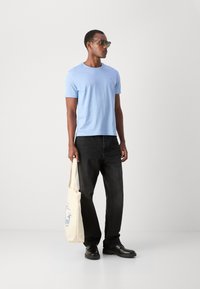 Light blue cotton t-shirt, black straight-leg jeans, black shoes, and a cream tote bag with blue graphic print. Sunglasses complete the outfit.