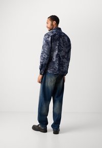 Navy patterned denim jacket with a structured collar and button closures, paired with loose blue jeans and black platform shoes.