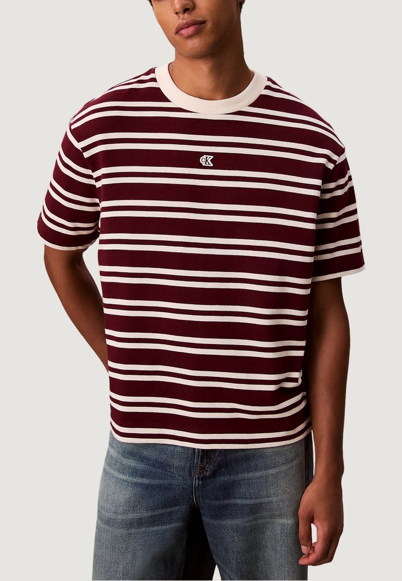 Tříčtvrteční tričko v pruhovaném designu v maroon a bílé barvě s ribbovaným kulatým výstřihem a malým logem na hrudníku. Bavlněný materiál s krátkými rukávy.