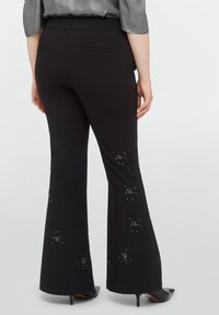 Black flared pants made of smooth fabric, featuring subtle rhinestone embellishments in star patterns along the lower sides and back pockets.