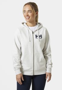 Sudadera con cremallera en gris claro, de tejido suave, que cuenta con un bolsillo canguro, puños acanalados y un logo impreso en el pecho en azul marino.