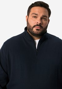 Námořnický modrý pulovr s vysokým límcem, se žebrovým polo zipem a jemnou, texturovanou tkaninou. Jednoduchý design bez dalších vzorů nebo akcentů.