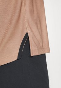 Camisa corta de mangas con color marrón claro, con aberturas laterales, combinada con tela negra en el dobladillo, que muestra una textura suave y costuras limpias.