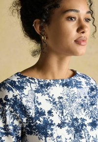 Ümarik teemandiga sinine ja valge lille- ja loomamuster. Omab paadi kaela lõiget ja tekstuurset kangast. Lihtsad kuldsed kõrvarõngad.