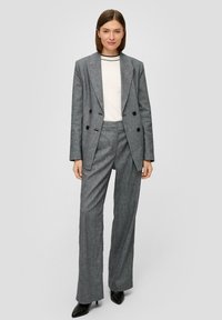 Costume gris à rayures comprenant un blazer croisé et un pantalon à jambes larges. Associé à un haut blanc et des bottes à talons noires.