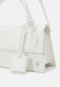 Sac à main en cuir synthétique blanc avec une forme structurée, une poignée supérieure et une bandoulière chaîne amovible. Comprend des détails de couture et un accent logo.