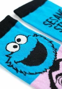 Calzini blu con polsini neri caratterizzati dal volto di un personaggio dei cartoni animati, che mostra grandi occhi e una bocca sorridente, con dettagli in rosa.