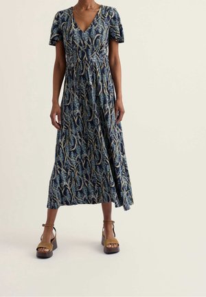 Femme portant une robe midi bleu marine avec un imprimé botanique, manches courtes, col en V et sandales compensées couleur tan avec des brides à la cheville.